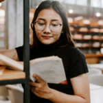 young woman in a library reading a book to build confidence