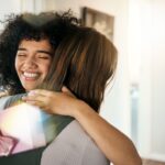 A woman greets another with a hug and gives her a gift.