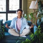 A woman meditates on her couch with headphones on.